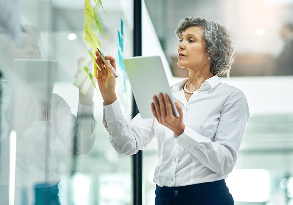 Woman writing on glass board with tablet.