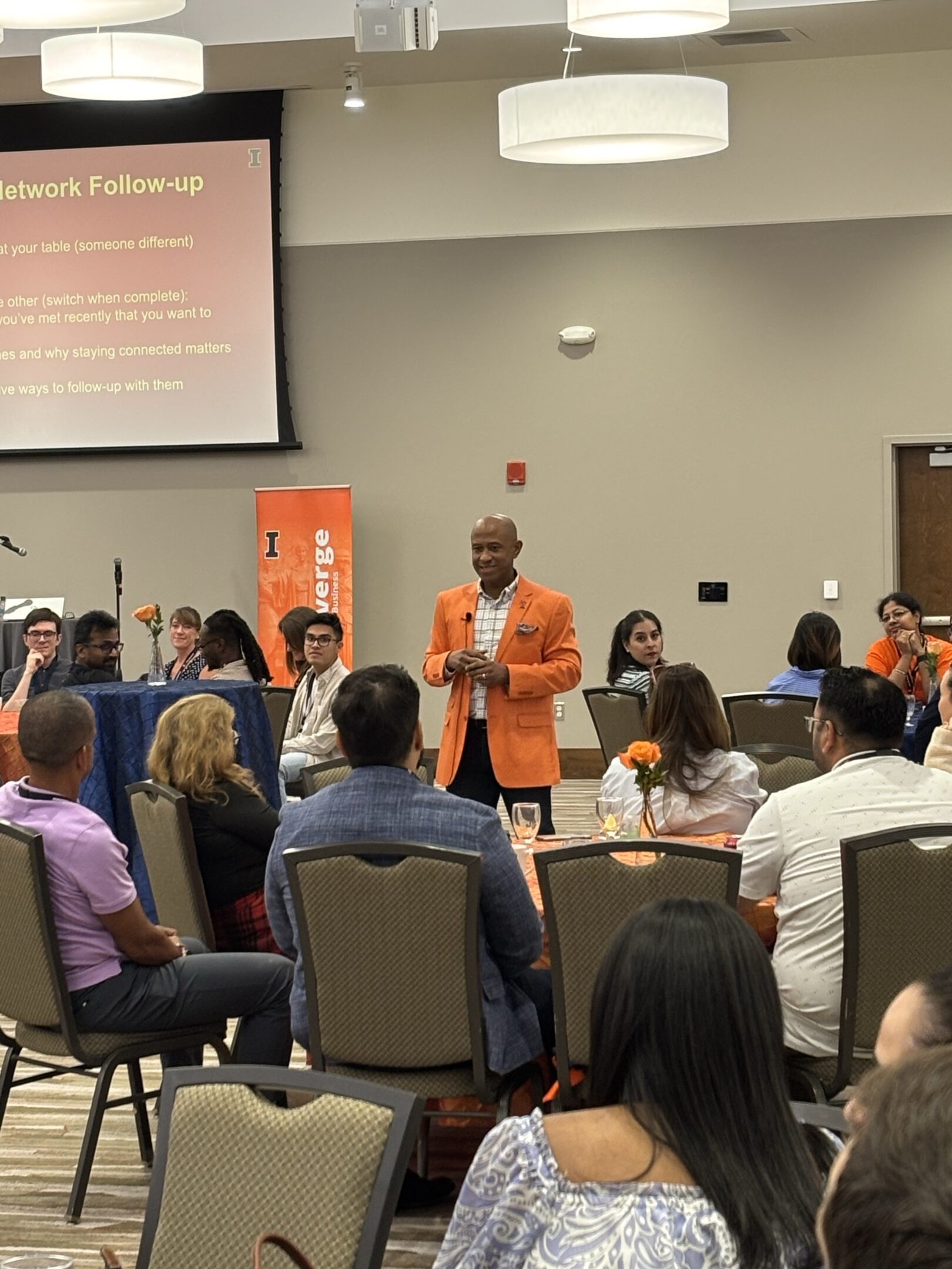 Speaker in orange blazer addressing seated conference audience