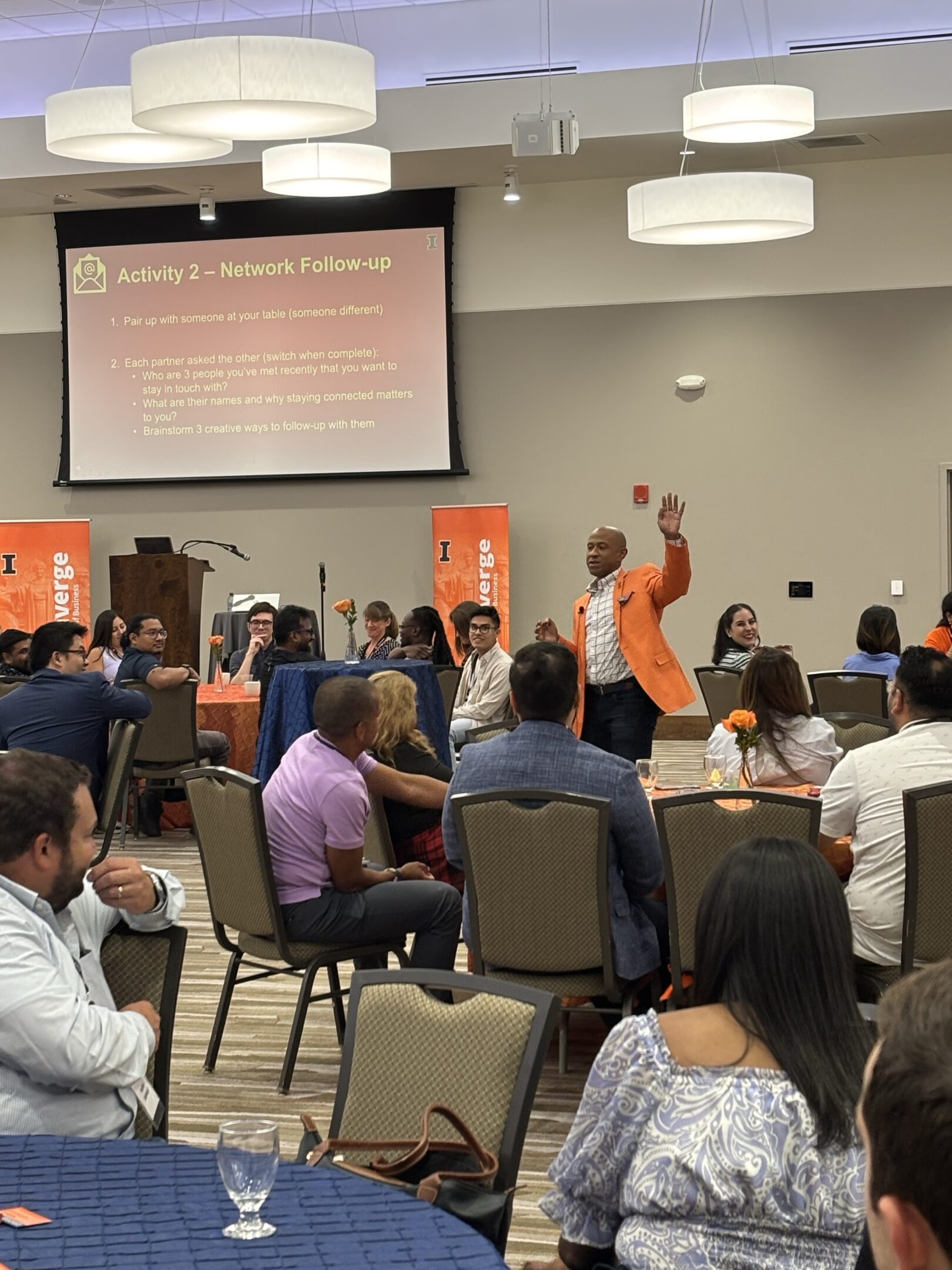 Speaker in orange jacket addressing seated audience