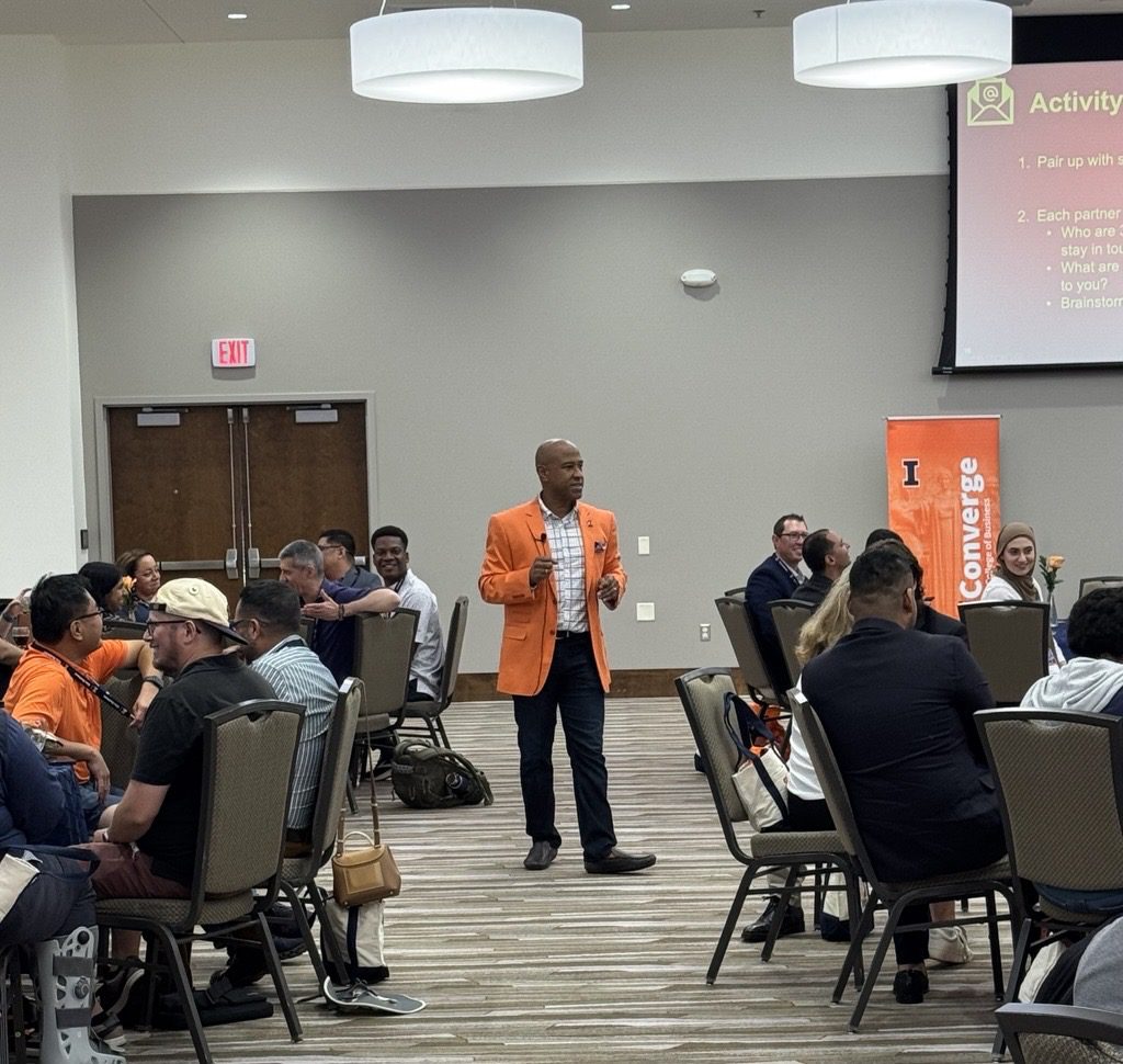 Speaker in orange blazer addressing seated conference audience