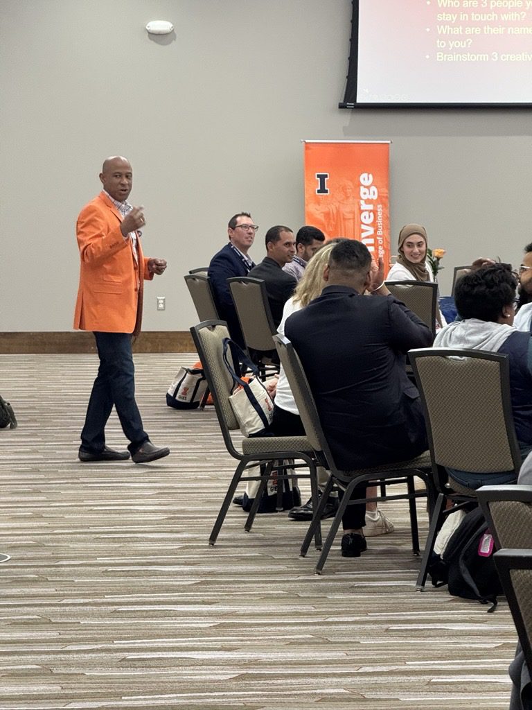 Speaker in orange blazer addressing seated conference attendees