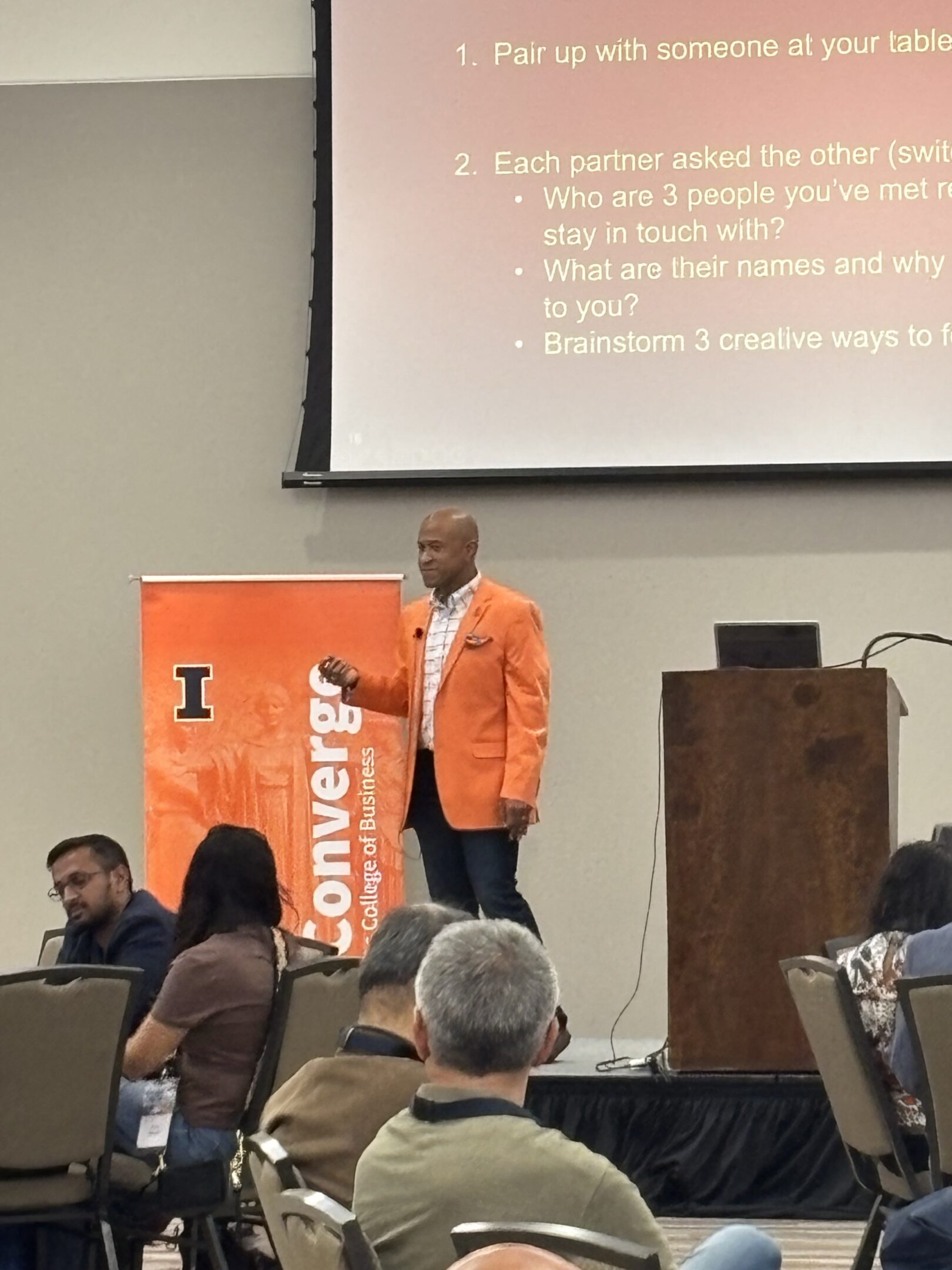 Speaker in orange blazer presenting to audience